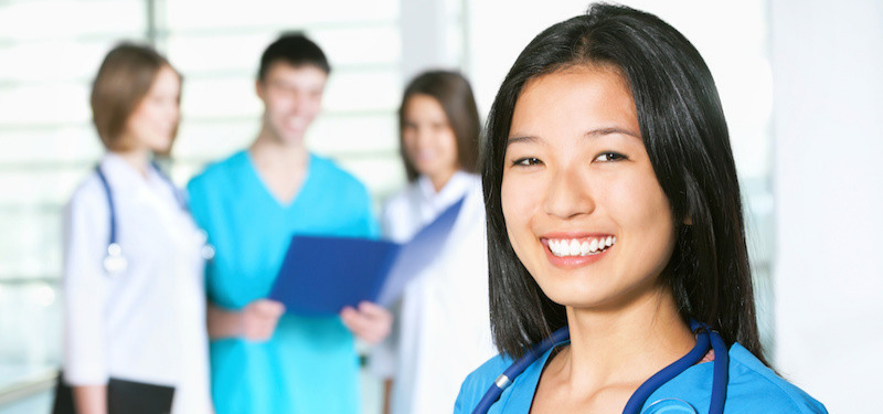 Dark Haired Nurse Smiling at Camera with People in the Background